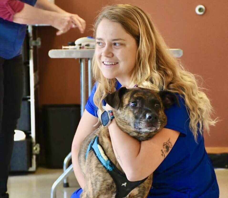 Sarah K. the Director of People, Pets and Vets hugging a brown dog at a veterinary clinic.